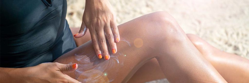 woman putting lotion on her legs at the beach