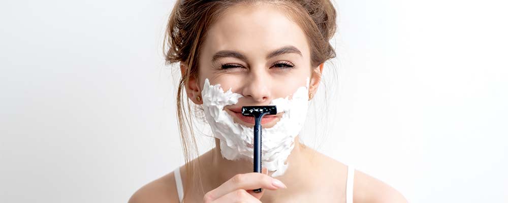 woman with shaving cream shaving her face with a razor